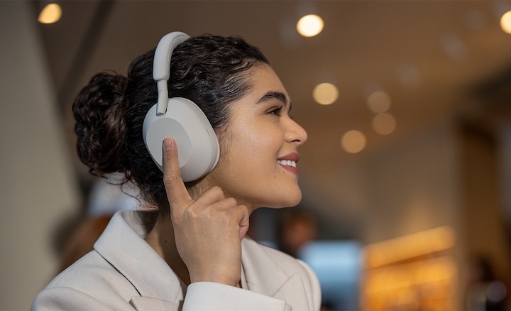 Una mujer que lleva unos audífonos WH-1000XM5 por la calle, tocando un audífono para activar los ajustes de control táctil