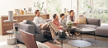 Familia en un sofá viendo la televisión con parlantes alrededor de la estancia que ofrecen una experiencia envolvente